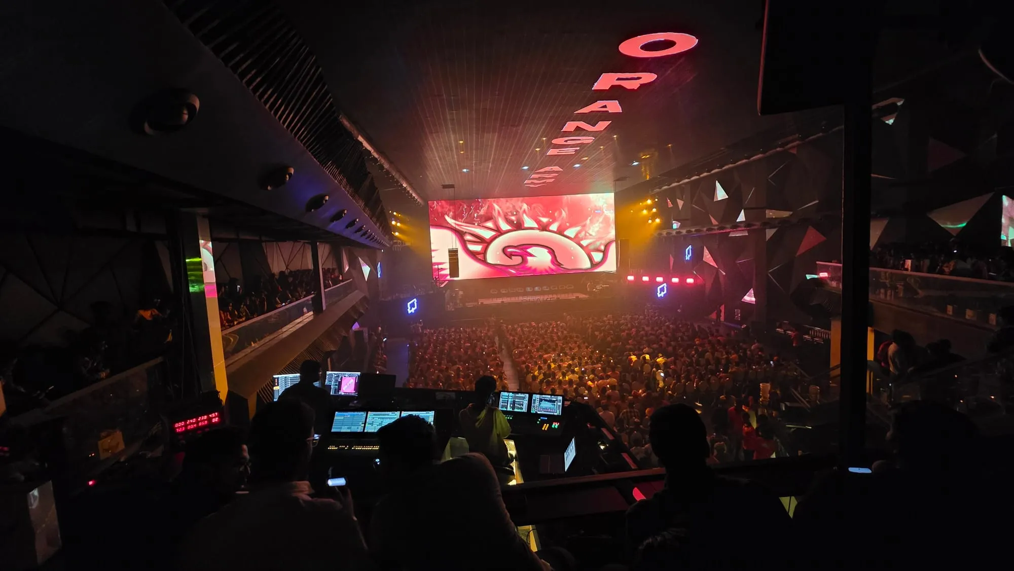 A crowd facing a large lit stage screen at a concert