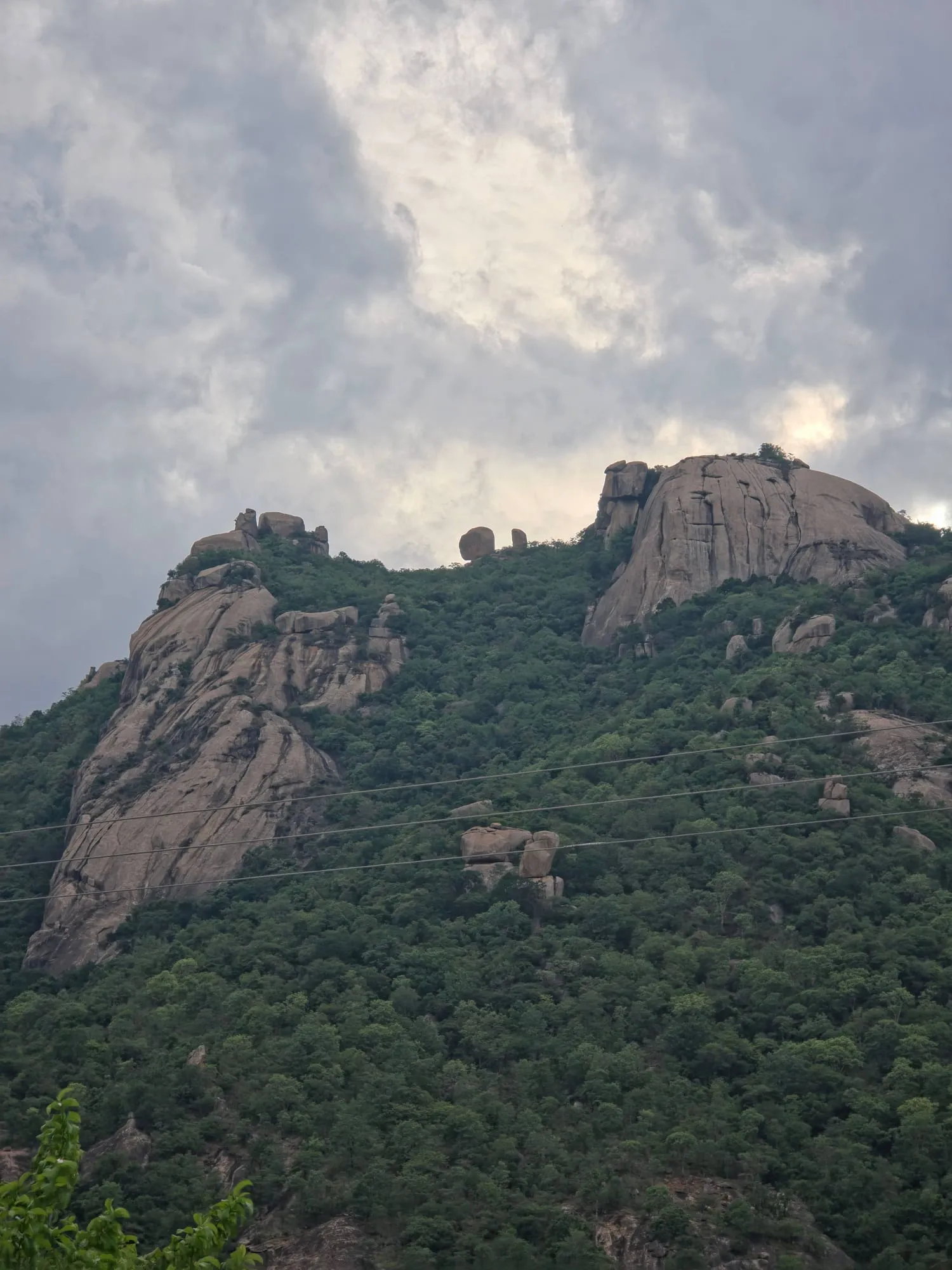 A rocky green hill under a cloudy sky